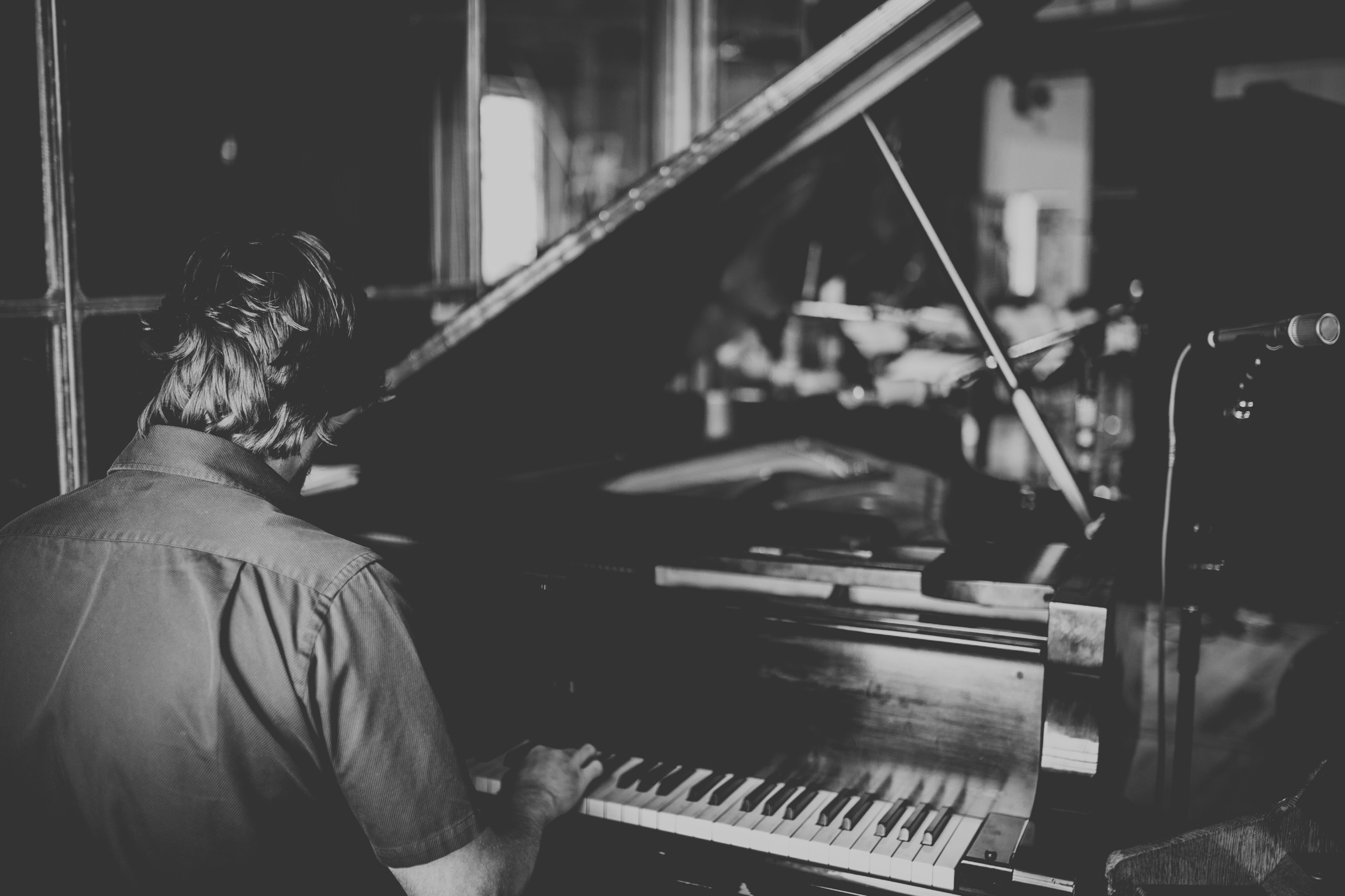 Monochromatic image of composer Jeff Toyne playing on grand piano.  His back is turned to camera. Background to piano pedigree of tracing back his piano training to Beethoven.
