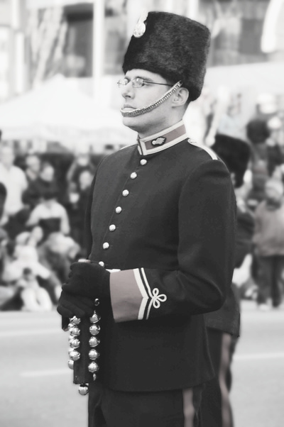 Close-up of composer Jeff Toyne as Bombadier, Band of the 15th Field Regiment, Royal Canadian Artillery.  He wears full dress uniform including bearskin with chin strap and tunic with brass buttons.