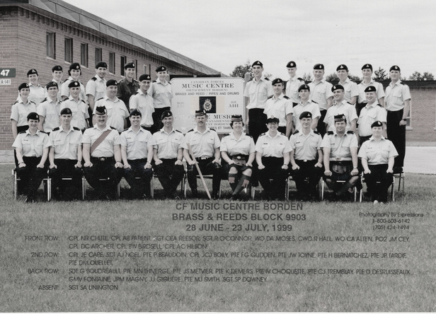 Group photo of composer Jeff Toyne with Band of the 15th Field Regiment. Sign indicates that this is the Canadian Forces Music Centre, Borden. Brass, reed, pipes, drums. His uniform is beret, white short sleeve shirt with epaulettes, dark trousers.