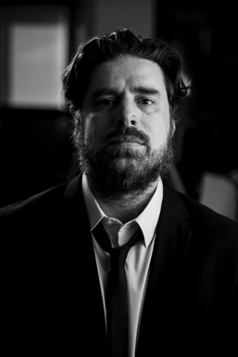 Portrait of composer, Jeff Toyne, by Kaori Suzuki. He is wearing a black suit and tie and white collared shirt. This image is not clickable.